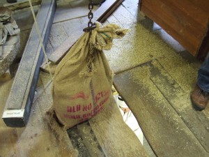 Bag of grain arrived via the hoist through a well-worn trapdoor. Miller visible on the floor below.