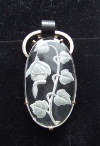 A fuschsia engraved on a glass, bakelite and white metal dress clip.