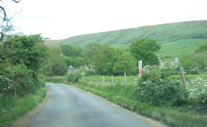 The approach to the village. Army 'keep out' sign to the right of the road.
