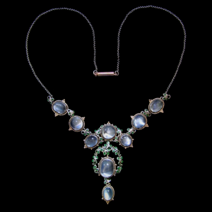 Jessie M King for Liberty & Co. A silver and gold necklace set with moonstones within borders of blue/green enamelled leaves surrounded by gold wire wirework and gold florets. The silver chain with a gold clasp. British. Circa 1900. Size: Height of drop pendant only 4.4 cm. Width 2 cm. Width across three moonstones 11 cm. Total length around necklace 41 cm. Sold by Van den Bosch.